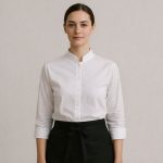 En kvinna i restaurangpersonal i vit skjorta med kinakrage och svart förkläde.