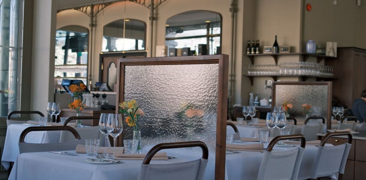 Ljus restaurangmatsal med dukade bord, textilstolar och avskärmande skärmar