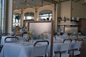 Ljus restaurangmatsal med dukade bord, textilstolar och avskärmande skärmar