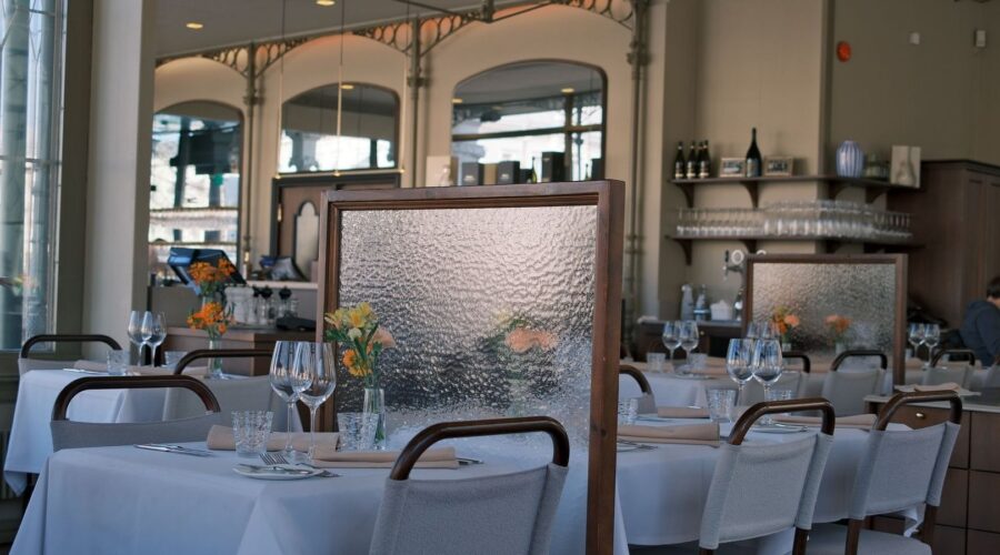 Ljus restaurangmatsal med dukade bord, textilstolar och avskärmande skärmar